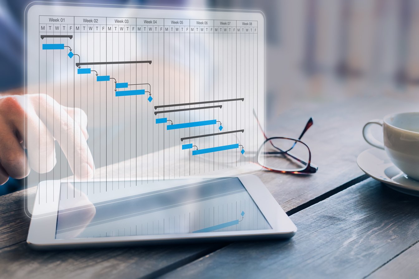 Project manager updating progress and deliverables milestones schedule on gantt chart planning with digital tablet computer, professional planner in office